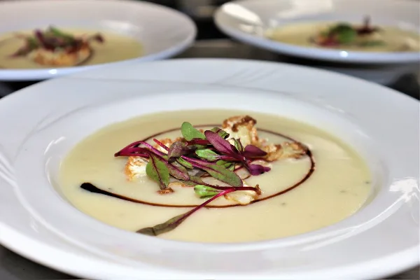 Multiple white plates holding a creamy soup or sauce dish topped with microgreens and garnish, arranged for service.