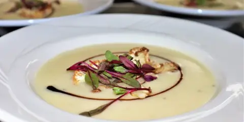 Multiple white plates holding a creamy soup or sauce dish topped with microgreens and garnish, arranged for service.