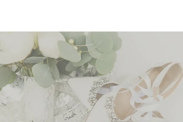 A white wedding bouquet with eucalyptus leaves resting next to a pair of white, beaded bridal shoes.