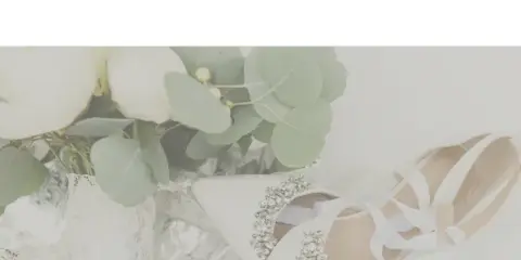 A white wedding bouquet with eucalyptus leaves resting next to a pair of white, beaded bridal shoes.