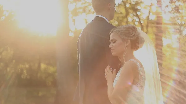 A bride and groom standing together in a sunlit outdoor setting, captured in a cinematic style.