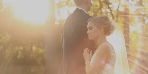 A bride and groom standing together in a sunlit outdoor setting, captured in a cinematic style.