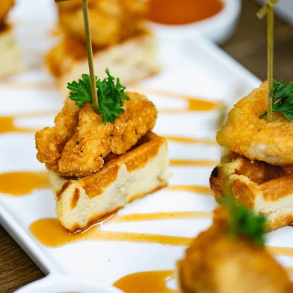 Close-up of a plated appetizer featuring fried food on bread with a sauce drizzle and parsley garnish.