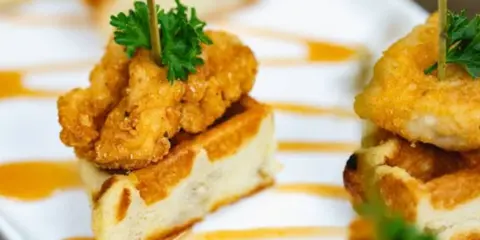 Close-up of a plated appetizer featuring fried food on bread with a sauce drizzle and parsley garnish.