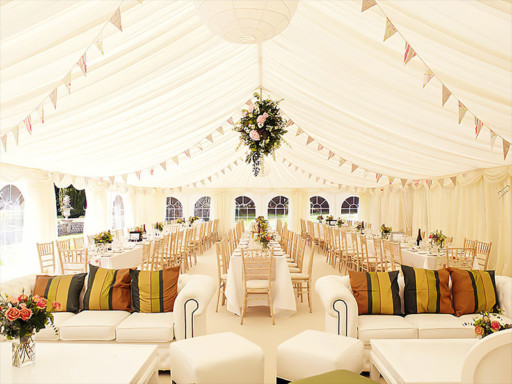Interior of a white wedding tent featuring long reception tables, chairs, and floral decorations.