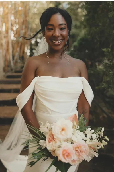A smiling bride with a styled updo and makeup holding a bouquet of flowers.