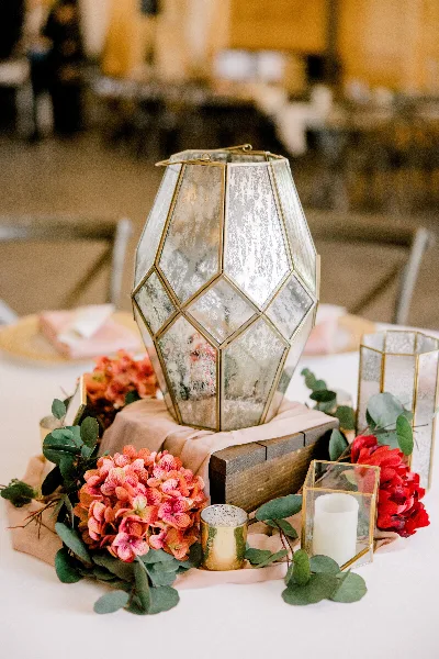 A wedding table centerpiece featuring a geometric mirrored lantern, pink linens, and floral arrangements.