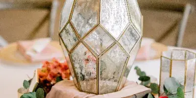 A wedding table centerpiece featuring a geometric mirrored lantern, pink linens, and floral arrangements.