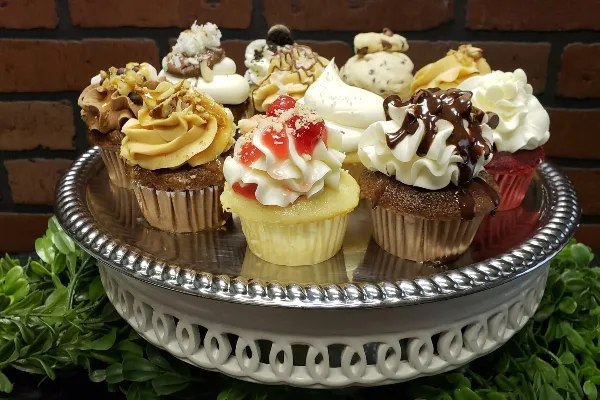 An assortment of decorated cupcakes with various frostings and toppings arranged on a silver cake stand.
