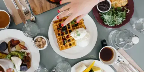 Overhead view of a table set with various catering dishes including waffles, shakshuka, and a breakfast platter.