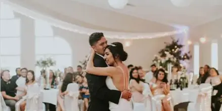 A bride and groom dancing during a wedding reception in a large ballroom with guests seated at tables.
