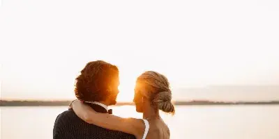 A bride and groom embracing at sunset by a body of water.