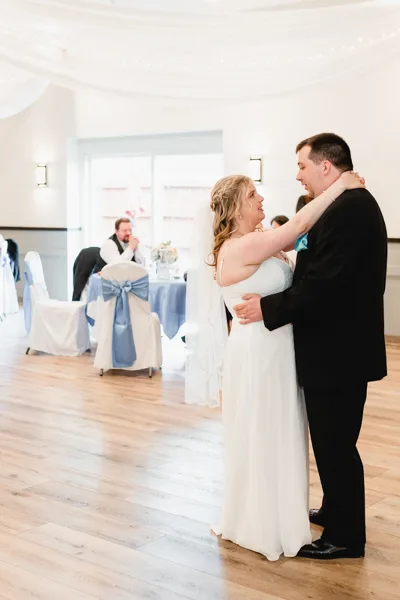 A bride and groom dancing in a wedding reception hall with decorated tables and chairs.