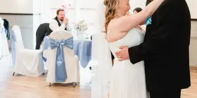 A bride and groom dancing in a wedding reception hall with decorated tables and chairs.