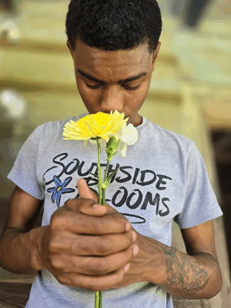 A young man wearing a Southside Blooms t-shirt holds a yellow and white flower stem.