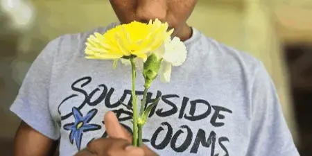 A young man wearing a Southside Blooms t-shirt holds a yellow and white flower stem.