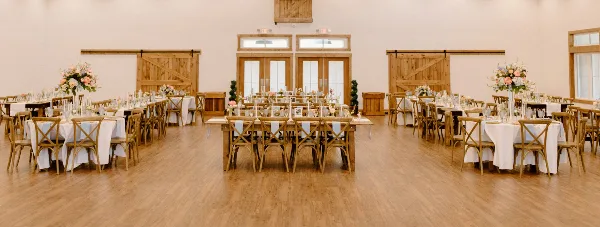 Interior view of the King Cole Farm Pole Barn reception space featuring long wooden tables, white linens, and floral centerpieces.