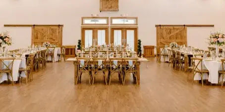Interior view of the King Cole Farm Pole Barn reception space featuring long wooden tables, white linens, and floral centerpieces.