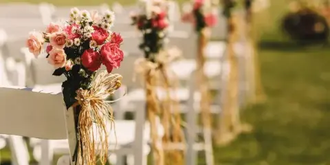 Outdoor wedding ceremony aisle with white chairs decorated with pink and red roses and burlap ties.