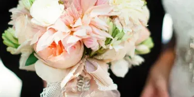 A close-up of a bridal bouquet with pink and white flowers and ribbons held by a couple.