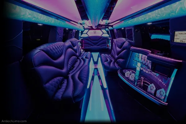 Interior of a luxury party bus with purple leather seating, blue and pink LED lighting, and a bar area.
