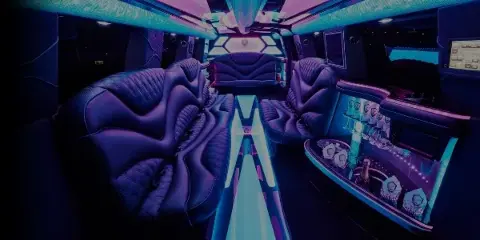 Interior of a luxury party bus with purple leather seating, blue and pink LED lighting, and a bar area.