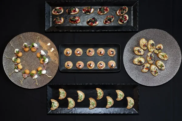 An overhead view of various gourmet appetizers and canapés arranged on black and silver serving platters.