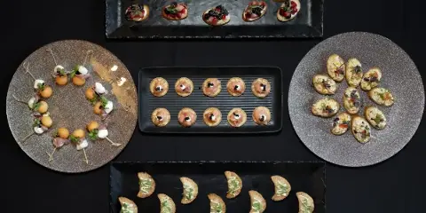 An overhead view of various gourmet appetizers and canapés arranged on black and silver serving platters.