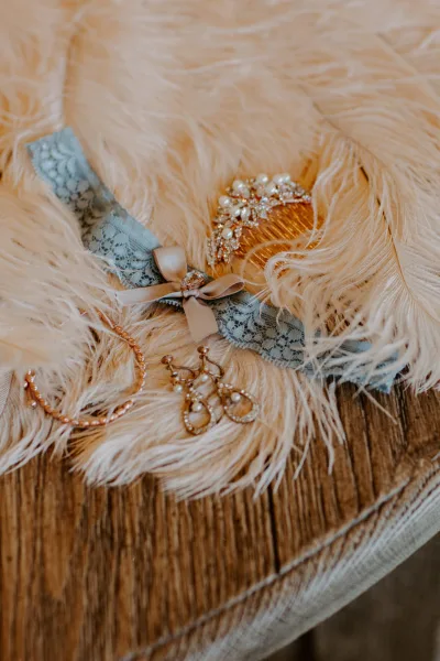 A wedding garter, pearl jewelry, and a decorative comb arranged on a fluffy beige surface.