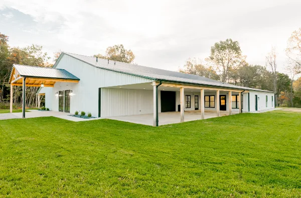 Exterior view of a white metal barn-style event venue with a covered porch and green lawn.
