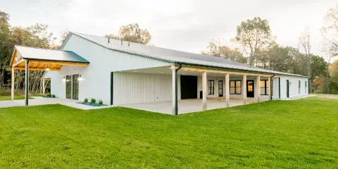 Exterior view of a white metal barn-style event venue with a covered porch and green lawn.