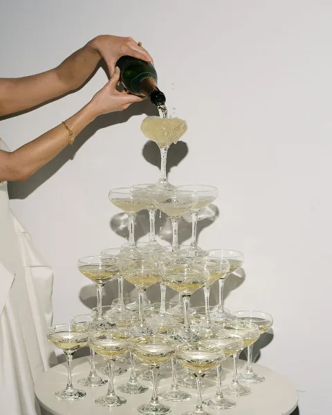 A person pouring champagne into a tiered glass tower at an event.