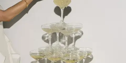 A person pouring champagne into a tiered glass tower at an event.