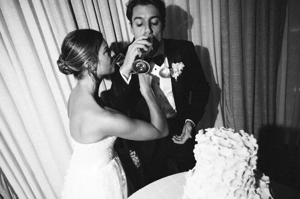 Black and white photo of a bride and groom drinking from wine glasses at a wedding reception.