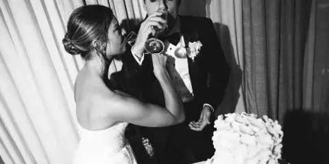 Black and white photo of a bride and groom drinking from wine glasses at a wedding reception.