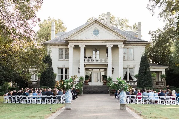 Exterior view of a white Greek Revival mansion with a wedding ceremony setup in the front yard.