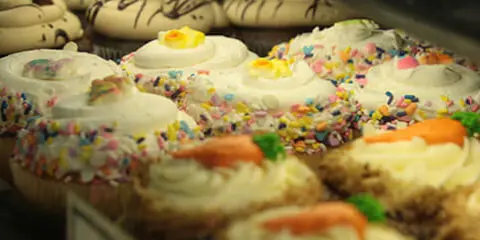 Assorted decorated cupcakes with frosting and sprinkles displayed in a bakery case