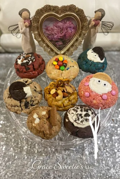 A glass stand holding an assortment of decorated cookies, including M&M cookies, Oreo cookies, and pretzel nut cookies, with a heart-shaped frame in the background.