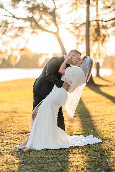 A bride and groom sharing a kiss in a grassy field during golden hour.