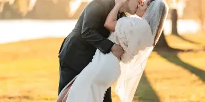 A bride and groom sharing a kiss in a grassy field during golden hour.