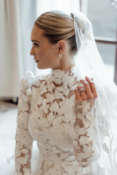 Bride in profile wearing a lace wedding dress and veil with styled hair and makeup