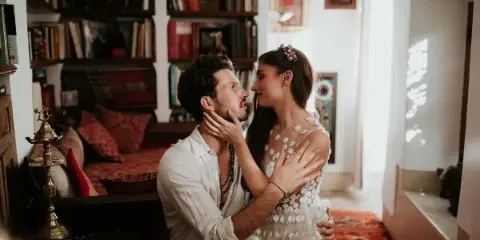 A bride and groom sharing an intimate moment in a room with bookshelves and warm lighting.