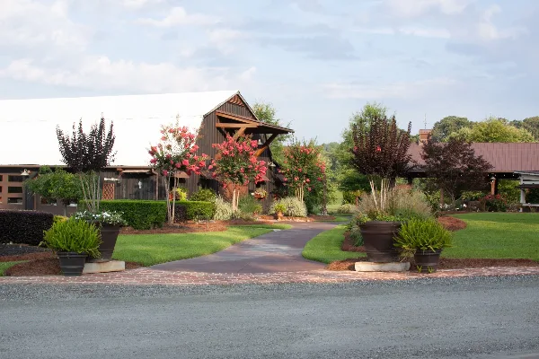 Exterior view of a rustic wooden barn wedding venue with a paved walkway and landscaped gardens.
