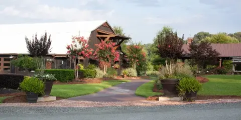 Exterior view of a rustic wooden barn wedding venue with a paved walkway and landscaped gardens.