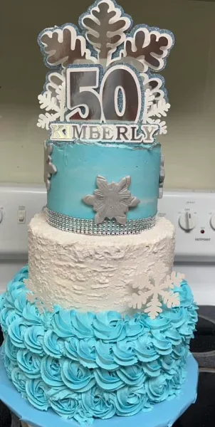 A three-tiered custom celebration cake featuring blue and white frosting, piped rosettes, and a '50' anniversary topper.