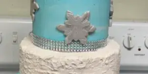 A three-tiered custom celebration cake featuring blue and white frosting, piped rosettes, and a '50' anniversary topper.