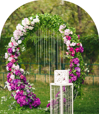 A floral wedding arch decorated with pink and purple roses and greenery, set outdoors on a lawn.