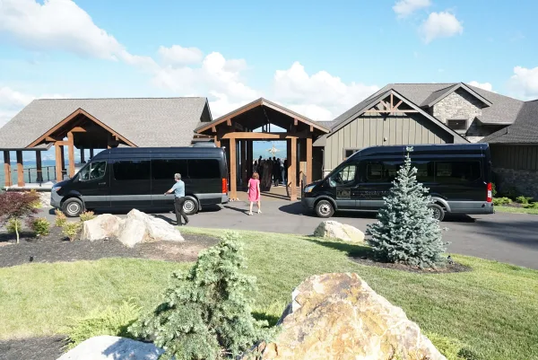 Two black passenger vans parked outside a lodge-style building with people walking toward the entrance.