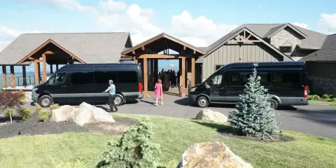 Two black passenger vans parked outside a lodge-style building with people walking toward the entrance.