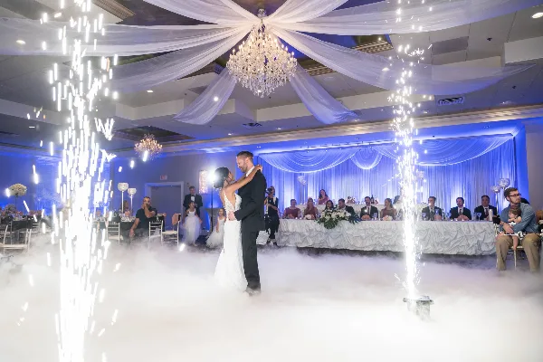 A bride and groom dancing in a large banquet hall with sparkler fountains and low fog effects.